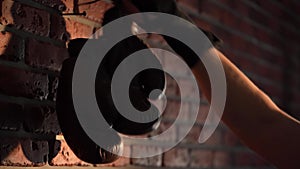 The shot shows a close up of a brick wall with a nail nailed to it on which boxing, brown gloves hang. The man then