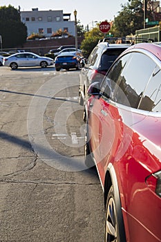 A shot of the side profile of a red Tesla Model 3 parked on a street with cars driving near a stop sign in Pasadena California