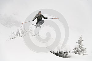 Shot of skier masterfully jumping in the air over a snow-covered mountain slope. Freeride skiing concept