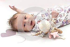 Shot of smiling baby in slips with wooden toy lying on a pink rug