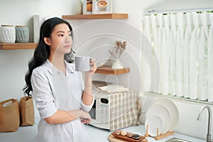 Shot of smiling young woman drinking a cup of coffee in the kitchen at home