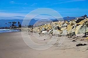 A shot of the smooth sand at the beach with large rocks along the sand near a large mountain range and RVs parked