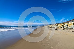 A shot of the smooth sand at the beach with large rocks along the sand near a large mountain range and RVs parked