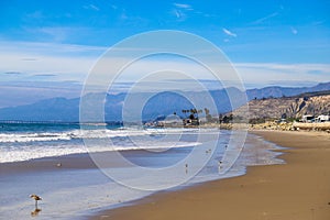 A shot of the smooth sand at the beach with large rocks along the sand near a large mountain range and RVs parked