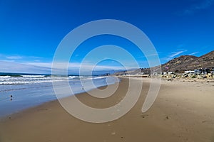 A shot of the smooth sand at the beach with large rocks along the sand near a large mountain range and RVs parked