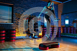 Shot of sporty young woman using step platform at gym. Aerobic and fitness exercises.