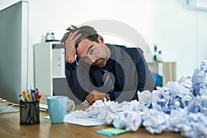 Work just keeps piling up. Shot of a stressed out businessman sitting at his desk overwhelmed by paperwork.