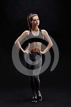 Shot of a strong woman with muscular abdomen in sportswear. Fitness female model posing on black background.