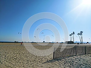 A shot of a sunny day at the beach with people flying kites and blue sky