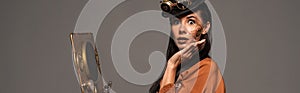 Shot of surprised steampunk woman using vintage laptop isolated on grey