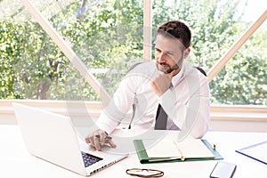 Shot of thinking businessman sitting at desk and using laptop while working at the office