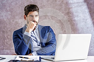 Shot of thinking businessman using laptop while sitting in the office and working