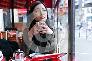 Thoughtful young asian woman drinking coffee in the terrace of a coffee shop.