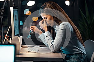 Tired business woman with neck pain looking uncomfortable while working with computer in the office at night