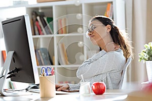 Tired young business woman having neck and back pain while working with computer in the office