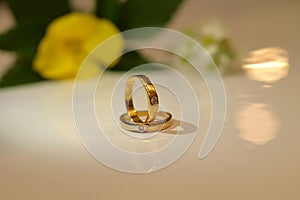 Shot of two golden wedding rings on a white surface decorated with fresh flowers in the backdrop