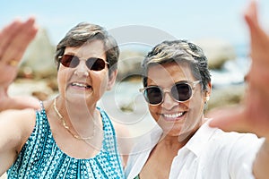 How can we not a selfie on the beach. Shot of two mature friends standing together and posing for a selfie during a day