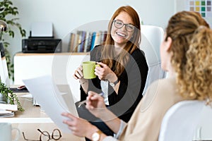 Two pretty young business woman relaxing one moment while drinking coffee in the office.