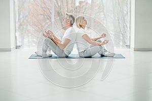 Shot of two senior people doing yoga in the class. Fitness people sitting on the exercise mat and relaxing in yoga position. Group