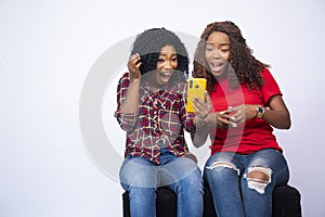 Shot of two young black females looking at the phone together feeling excited and surprised