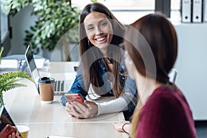 Two young business women friends working together with laptop while talking in the office at home