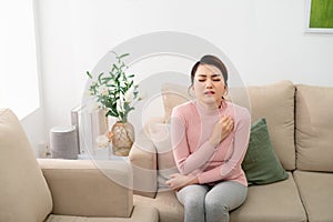 Shot of uncomfortable young woman scratching her arm while sitting on the sofa at home