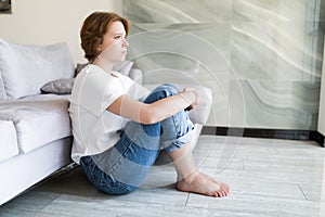 Portrait of unhappy lonely and depressed young woman hiding her face between legs at home