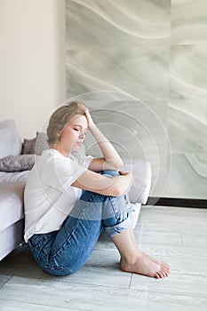 Portrait of unhappy lonely and depressed young woman hiding her face between legs at home