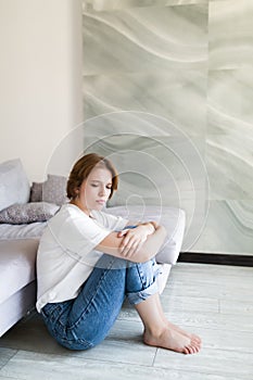 Portrait of unhappy lonely and depressed young woman hiding her face between legs at home