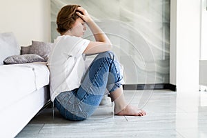 Portrait of unhappy lonely and depressed young woman hiding her face between legs at home