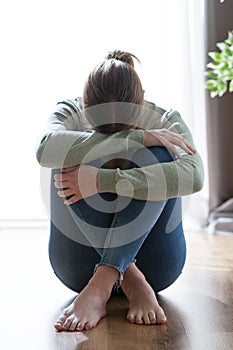 Unhappy lonely and depressed young woman hiding her face between legs at home.