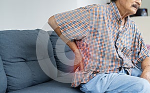 Shot of unhappy senior Asian man suffering from pain in back or reins at home