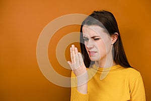 Shot of unhappy young woman checking her breath with hand, smells something awful, pinches nose, frowns in displeasure