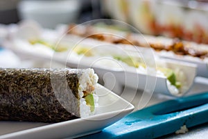 Shot of an unsliced sushi in white plate with blurred background of food