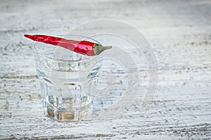 Shot of vodka with pepper on an old wooden table