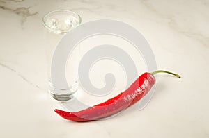 shot of vodka and red hot chili pepper on the bar/shot of vodka and red hot chili pepper on a white marble background. Selective
