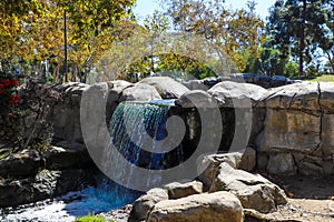 A shot of a waterfall over a stone lagoon into a river surrounded by lush green and autumn colored trees, plants with red berries