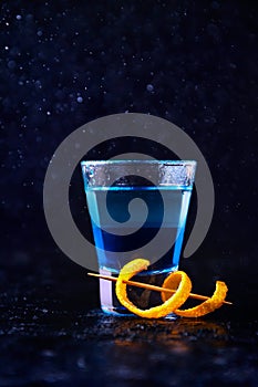 Shot with White Rum and Liquor Blue Curacao and Orange Peel. Alcoholic Layer Cocktail on Dark Background