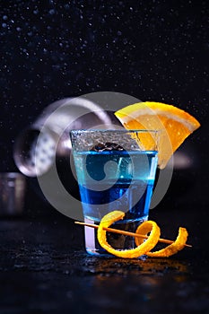 Shot with White Rum, Liquor Blue Curacao and Orange Slice. Alcoholic Layer Cocktail with Shaker on Dark Background