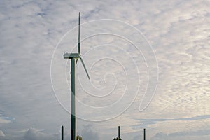 Shot of a wind turbine under cloudy blue sky. Smokestacks from a gas power plant in the background.