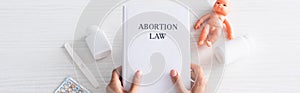 Shot of woman holding book with abortion lettering near baby doll and abortion pills