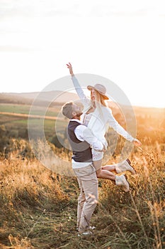 Shot of young boho hippie woman being carried by her handsome boyfriend in summer field. Couple having fun on their