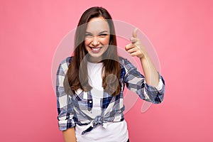 Shot of young happy smiling beautiful brunette woman with sincere emotions wearing trendy check shirt isolated on pink