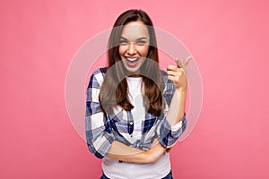 Shot of young happy smiling beautiful brunette woman with sincere emotions wearing trendy check shirt isolated on pink