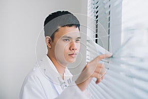 Shot of a young male doctor standing in doctor`s room and looking through the window