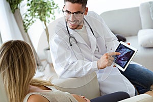 Young male gynecologist doctor showing to pregnant woman ultrasound scan baby with digital tablet.