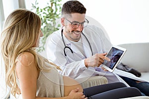 Young male gynecologist doctor showing to pregnant woman ultrasound scan baby with digital tablet.