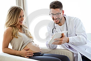 Young male gynecologist doctor showing to pregnant woman ultrasound scan baby with digital tablet.