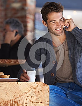 So good to hear from you again. Shot of a young man sitting in a cafe and talking on a cellphone.