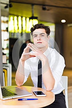 Shot of young man sitting at table looking at camera and thinking. Thoughtful businessman sitting home office. Sales man